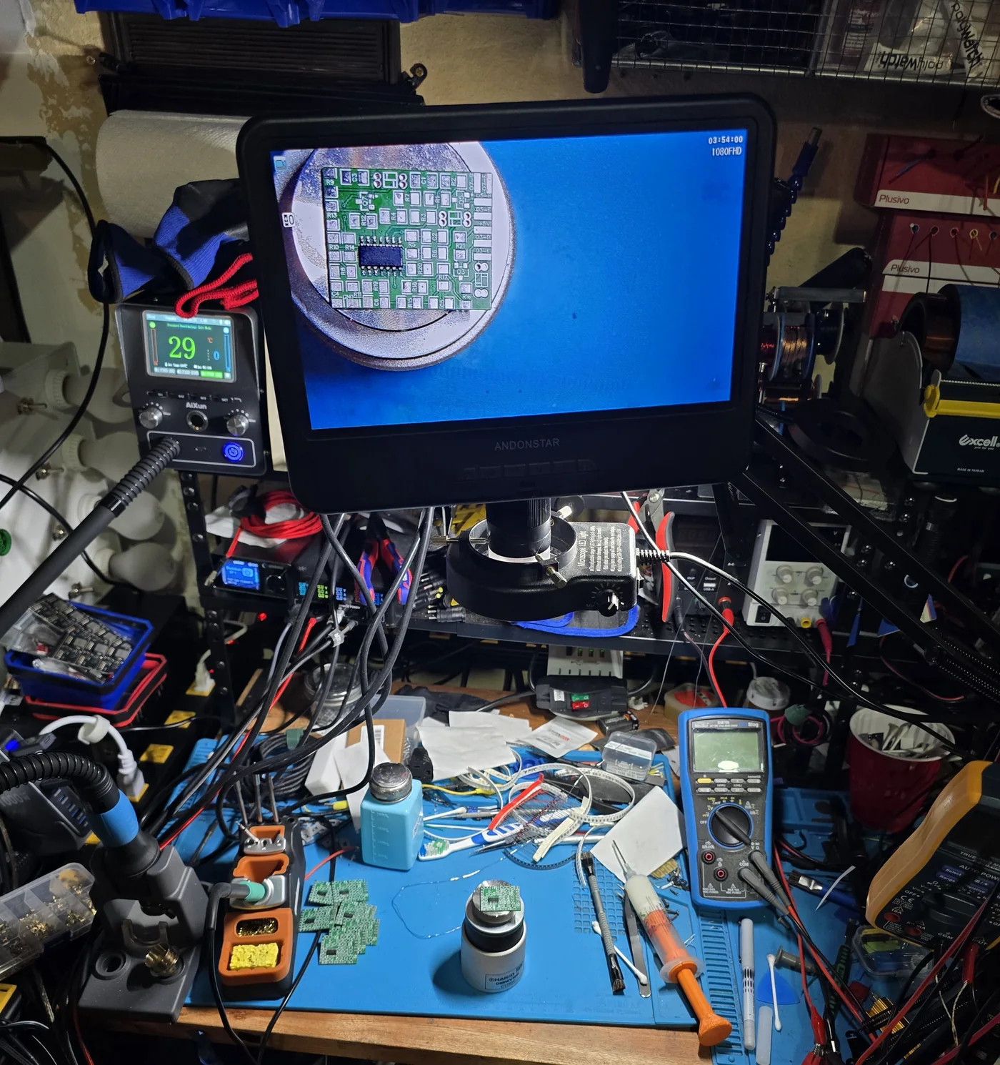 An Andonstar digital microscope on a swing arm above a workbench, its screen showing a magnified circuit board, with clear working space underneath.