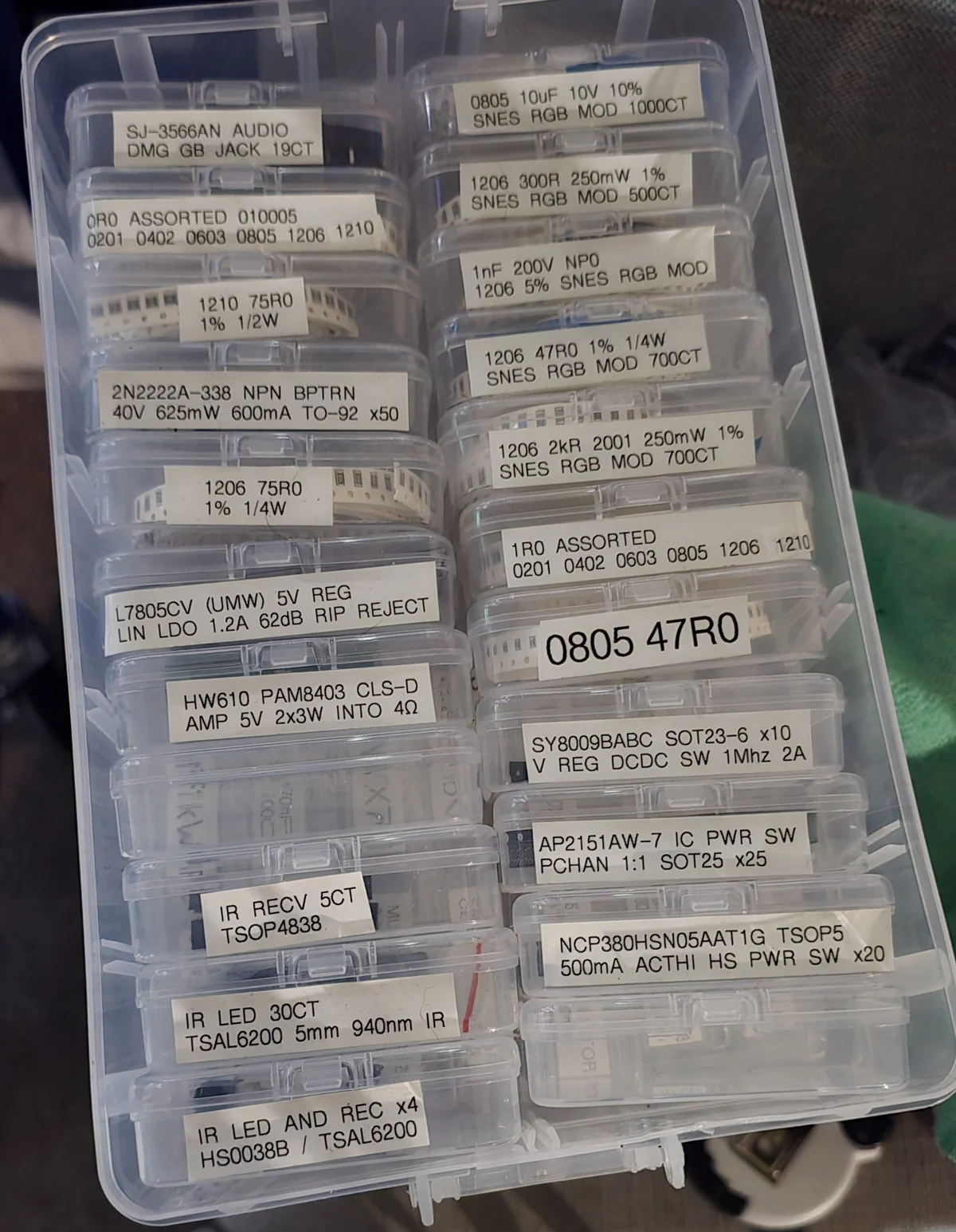 A parts organizer full of small snap-lid boxes, each with a printed label giving the part number, specifications, quantity and in some cases the project it is for.