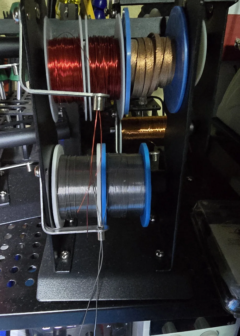 A benchtop stand holding reels of solder, wire and desoldering wick.