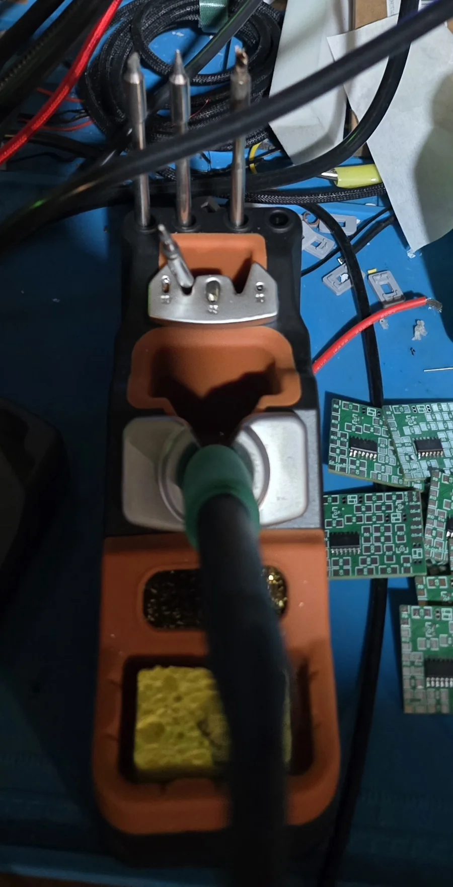 A soldering iron resting in its holder with three spare JBC-style tips standing upright beside it, next to brass wool and a sponge.