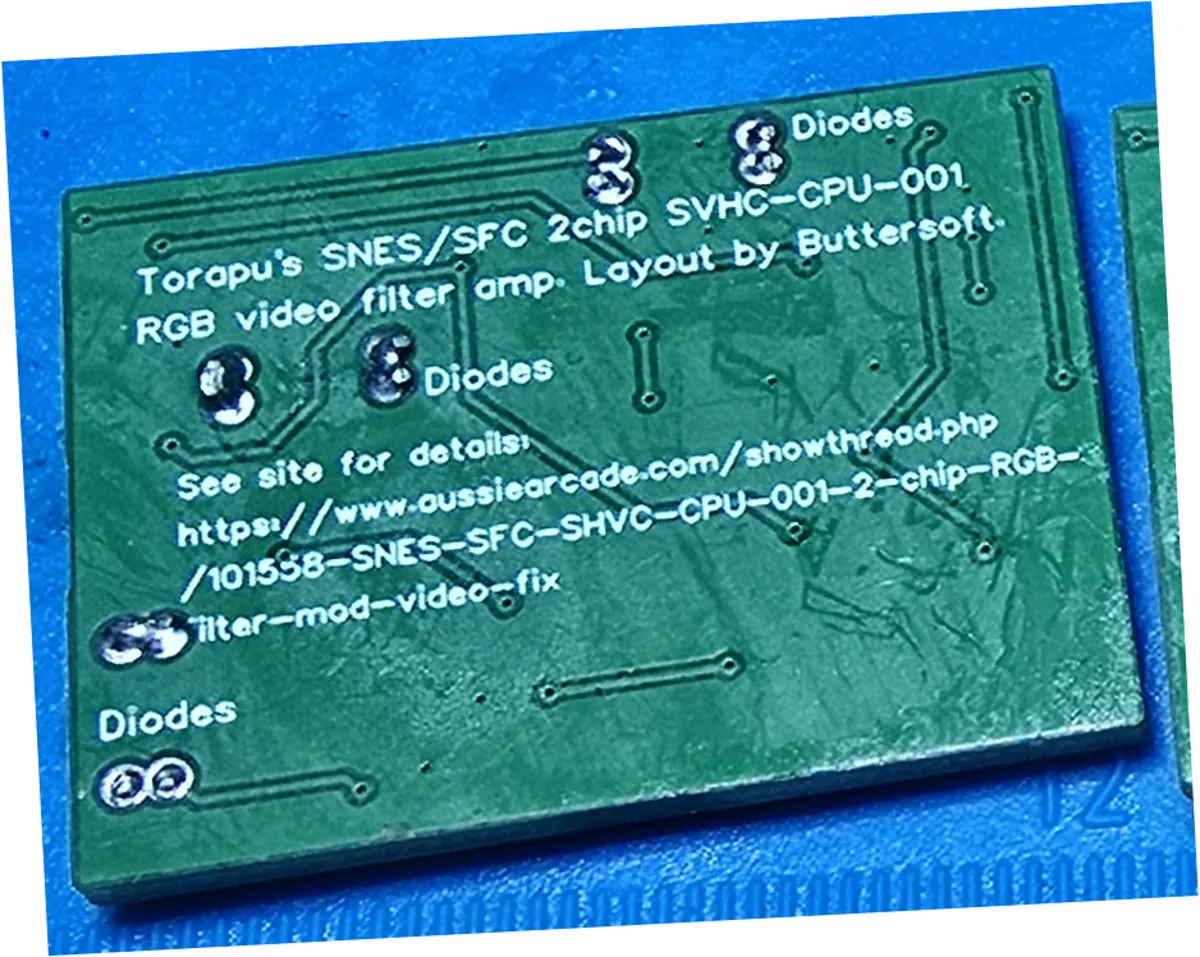 The same solder side of the same green circuit board after ultrasonic cleaning, photographed at the same angle and magnification. The solder mask is an even matte green across the whole board with no white film or streaking, the silkscreen text is crisp, and the through-hole pads are bright.