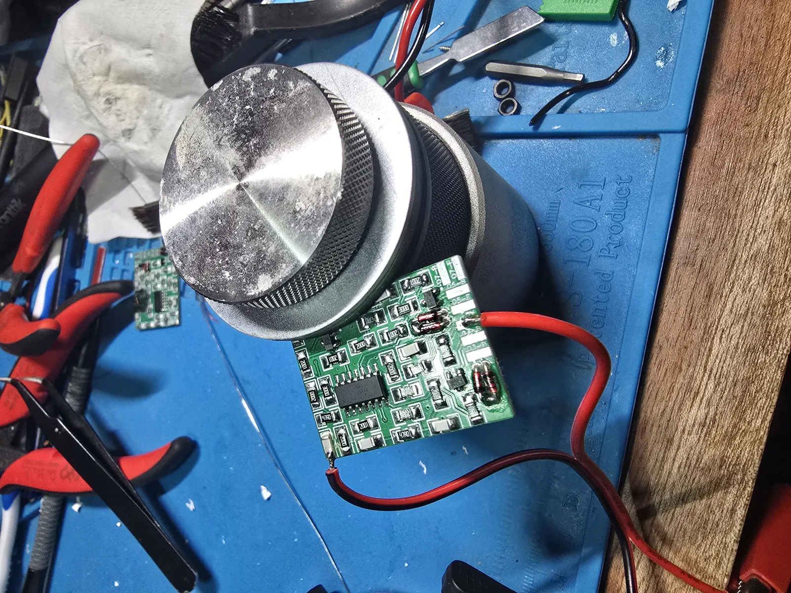 The finished mod board with red and black test wires soldered to its +5V and GND pads, ready for the bench supply.