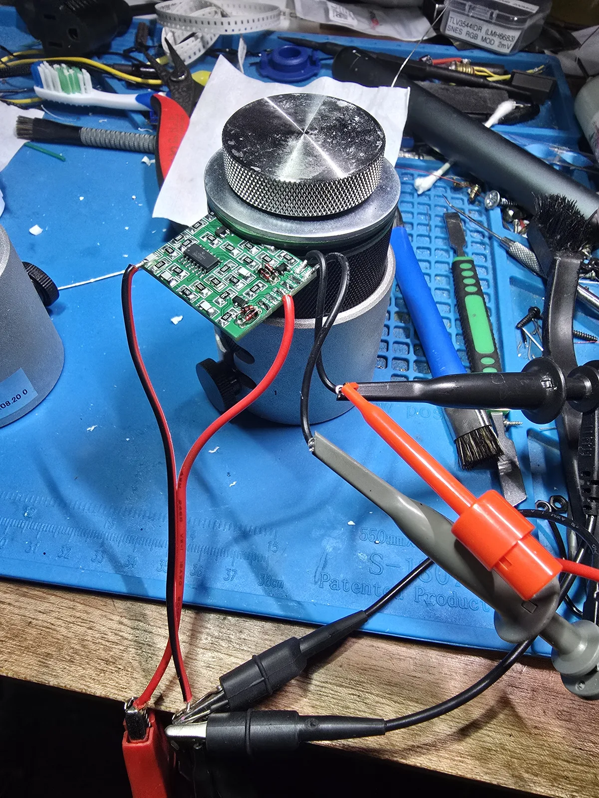 The mod board propped on a stand with power leads soldered to its +5V and GND pads and scope probe hooks clipped to the input and output pads.