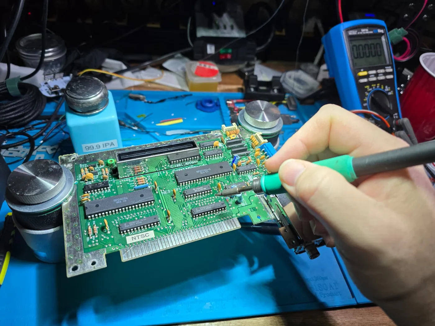 An NES front-loader mainboard on my bench, soldering iron in hand, multimeter alongside