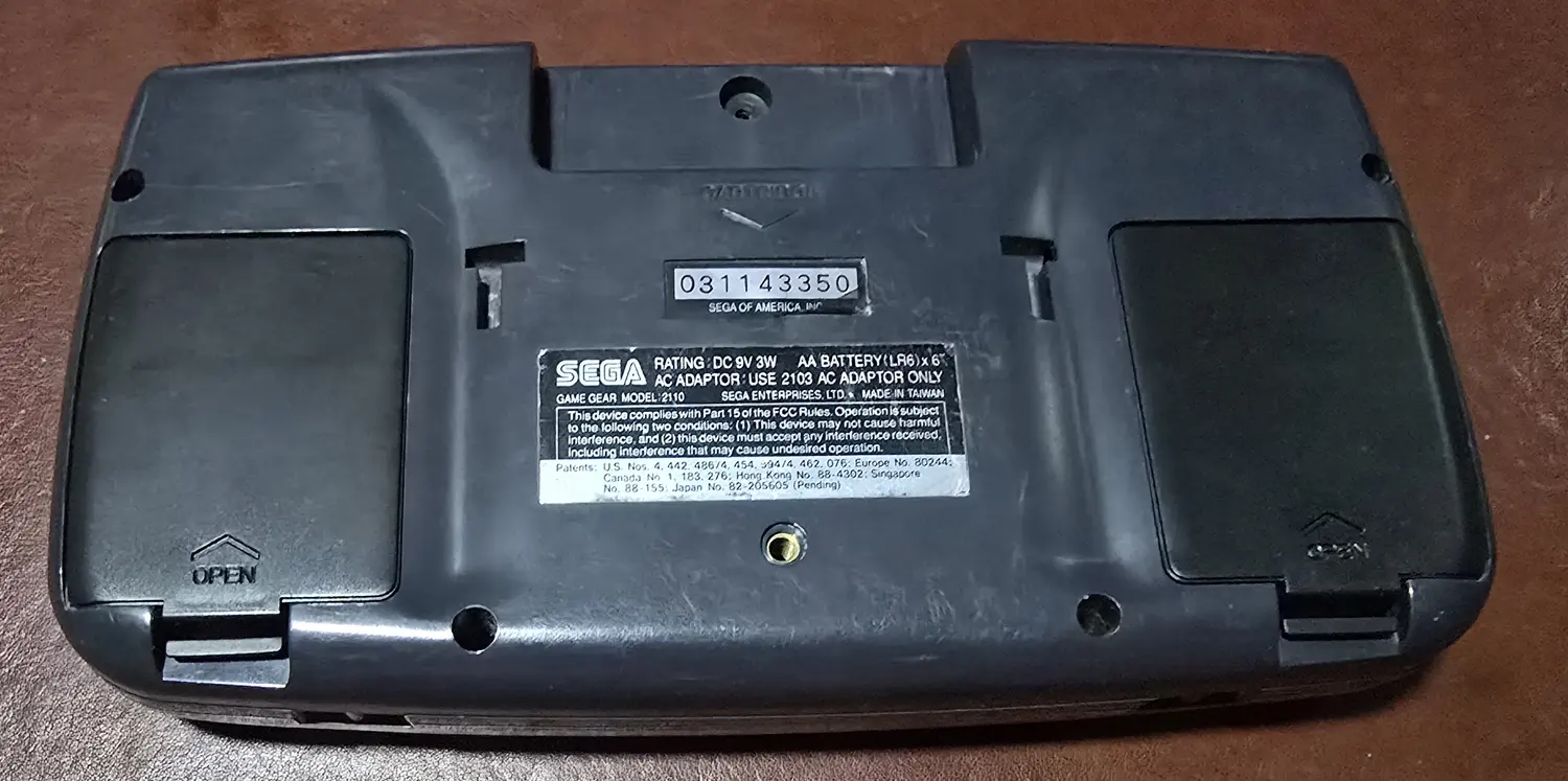 Back of the Game Gear with replacement battery doors fitted, serial 031143350 legible on the label