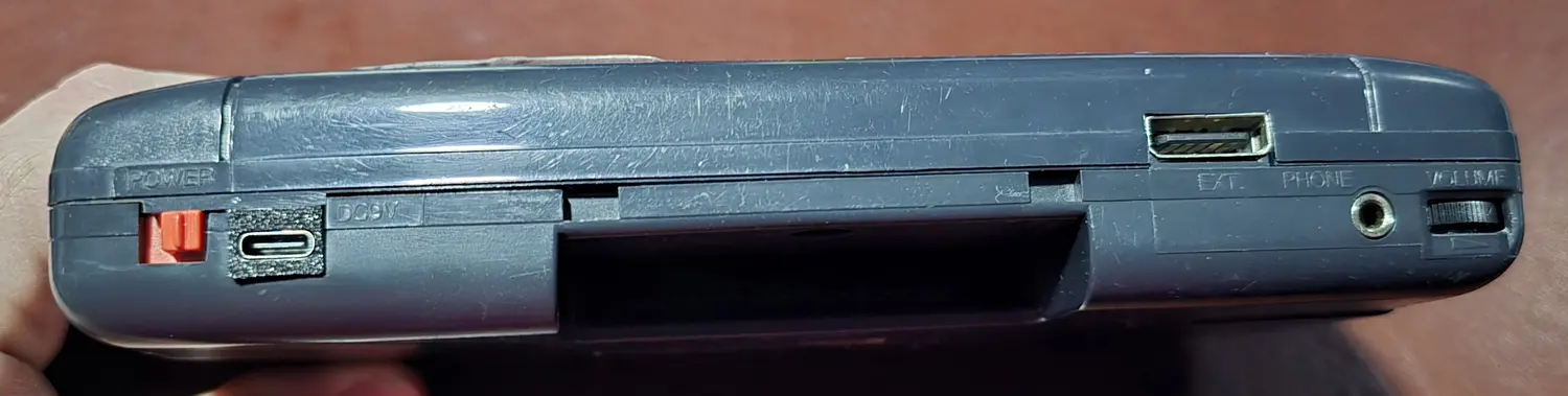 Top edge of the Game Gear showing a USB-C port fitted in the original DC jack position, next to the power switch, cartridge slot, EXT port, headphone jack and volume wheel