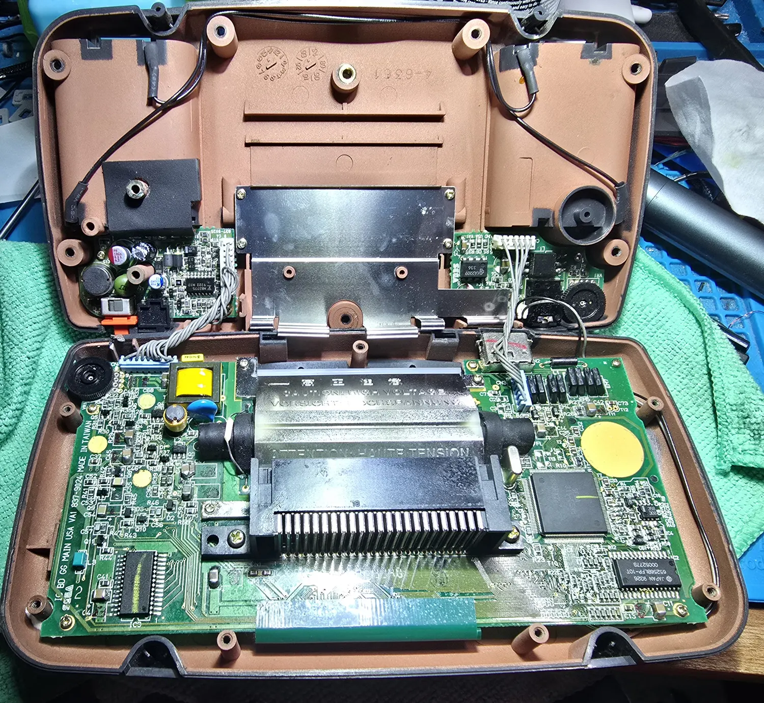 The Game Gear opened on the bench with both shell halves apart, showing the main board, sound board and power board