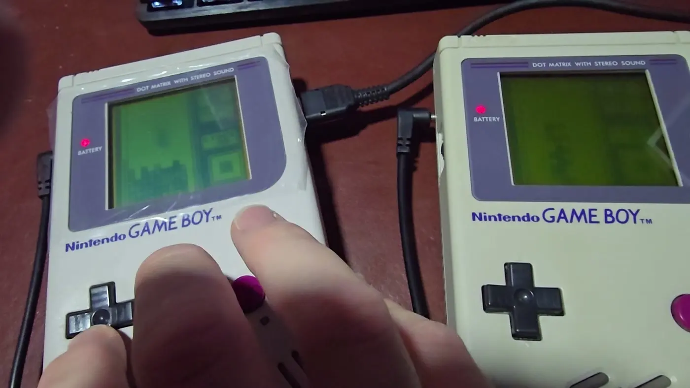 Two original Nintendo Game Boys linked together with a Game Link Cable, both powered on and running