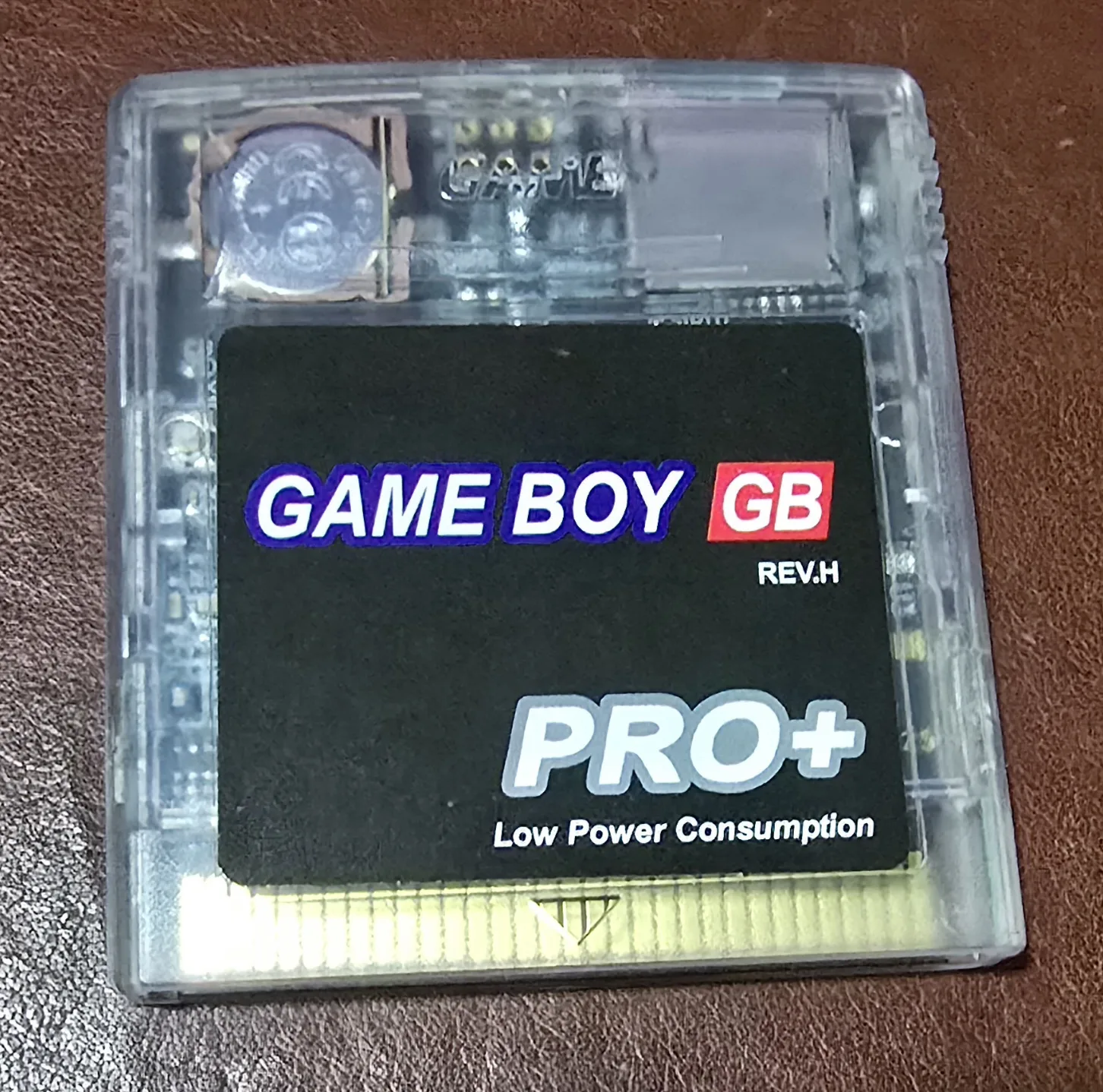 Front of the GB Pro+ microSD flash cartridge in a clear shell, the label reading GAME BOY GB REV.H PRO+ Low Power Consumption, with the coin cell and board visible through the plastic