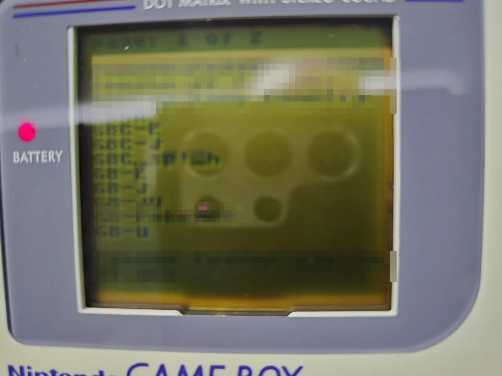 The flash cart's file browser running on the green screen of an original Nintendo Game Boy DMG-01, showing region folders and a page counter