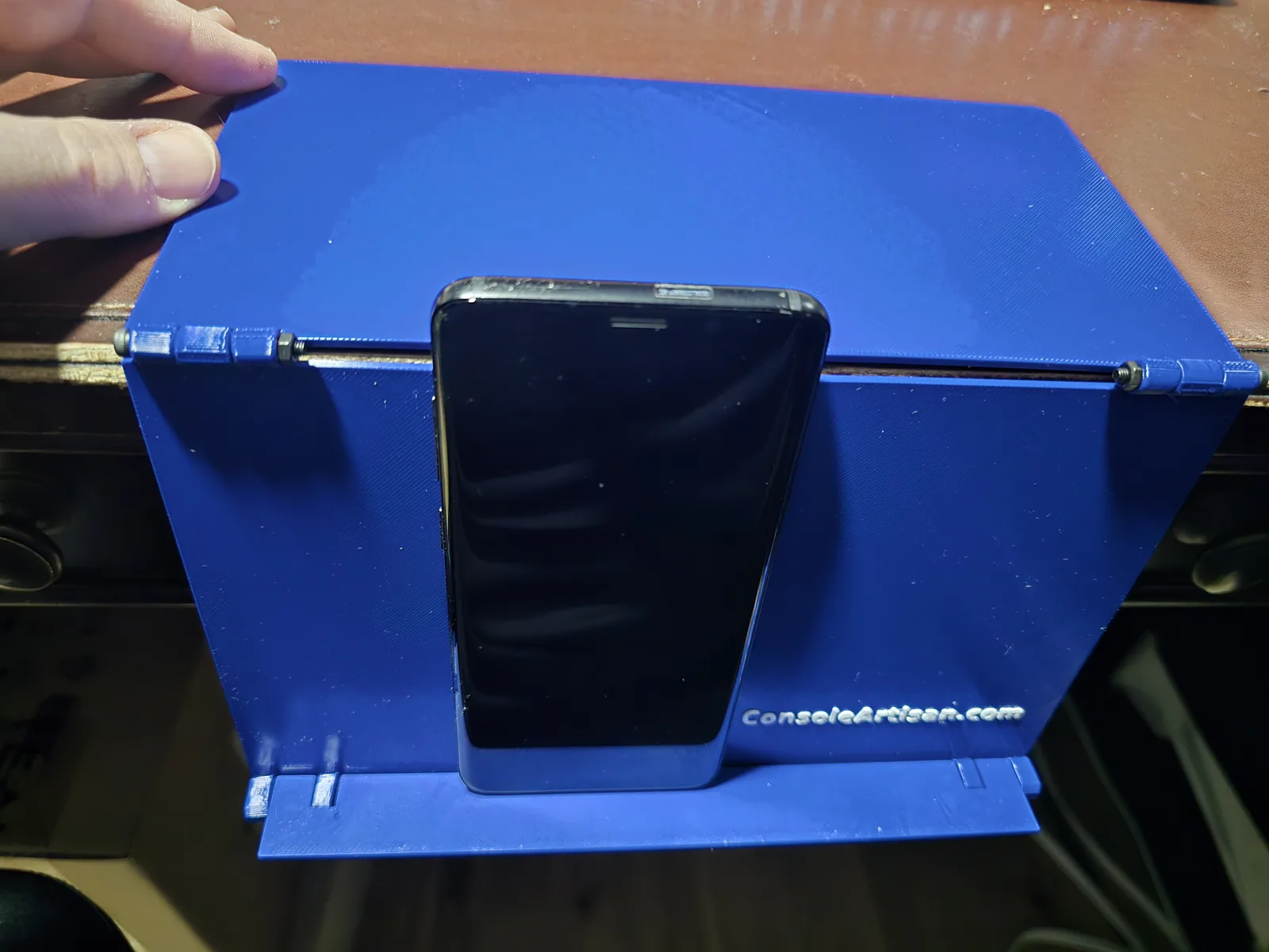 A phone standing on the Mahjong card holder's ledge, with a hand holding the top panel down