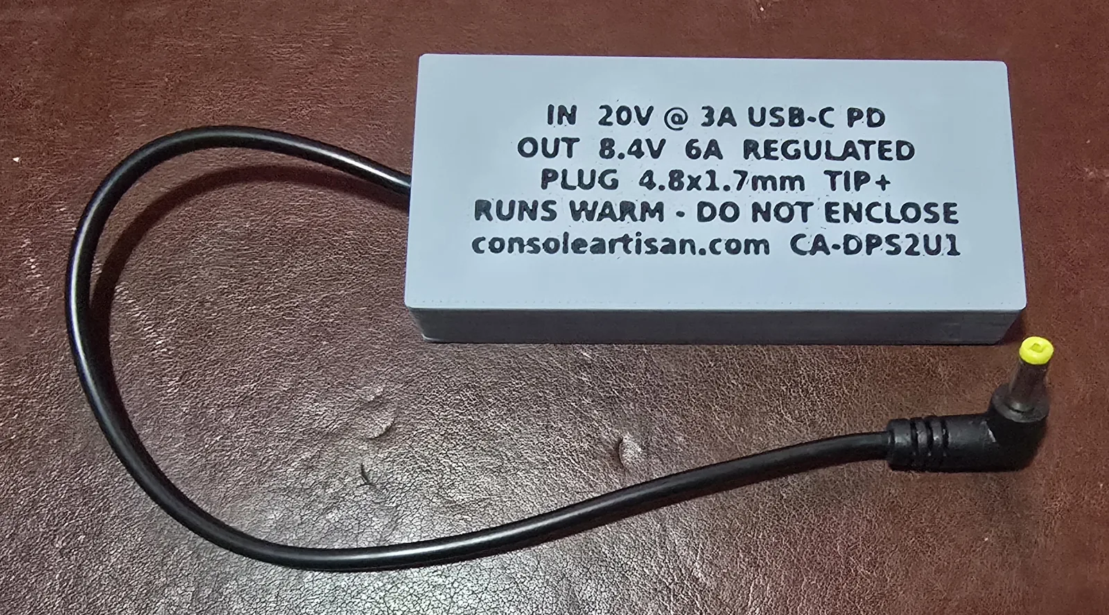 The back of the case, debossed with IN 20V at 3A USB-C PD, OUT 8.4V 6A REGULATED, PLUG 4.8 by 1.7mm TIP positive, RUNS WARM DO NOT ENCLOSE, consoleartisan.com CA-DPS2U1