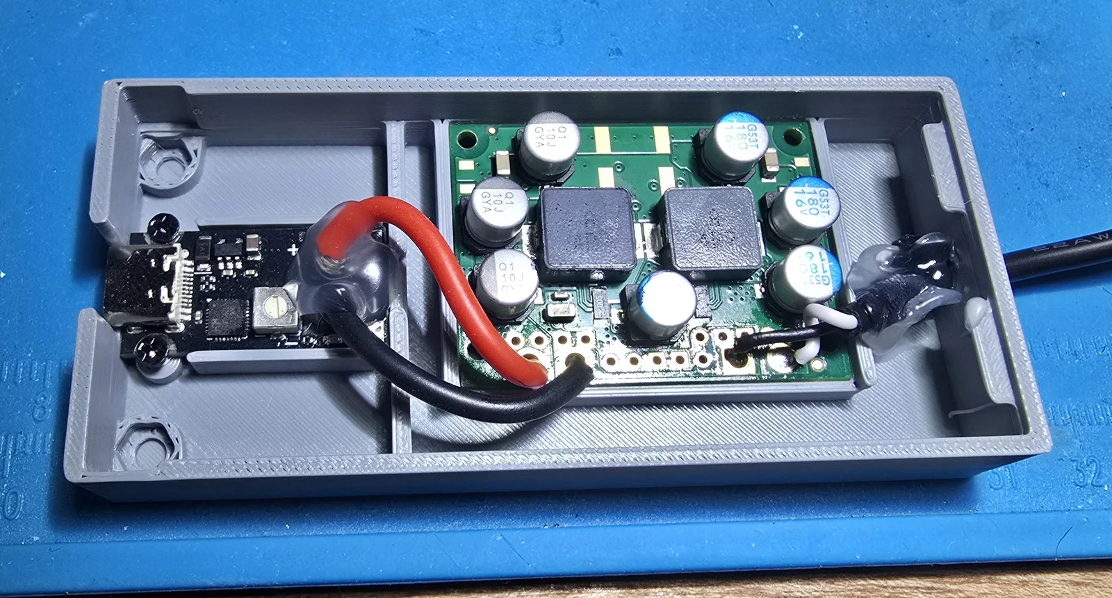 Close-up inside the finished unit showing clear adhesive beads over the wire joints at the trigger board and over the output cable where it leaves the case