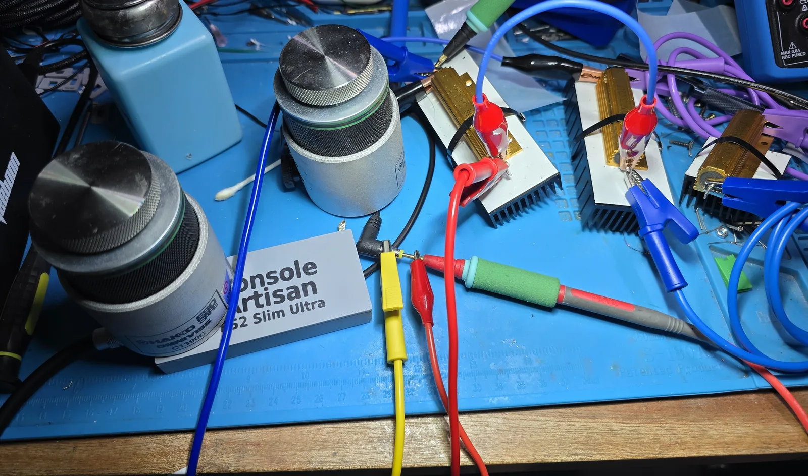 The sealed power supply on a workbench wired to a test rig of three large gold aluminium-housed power resistors bolted to heatsinks, with meters and test leads around it