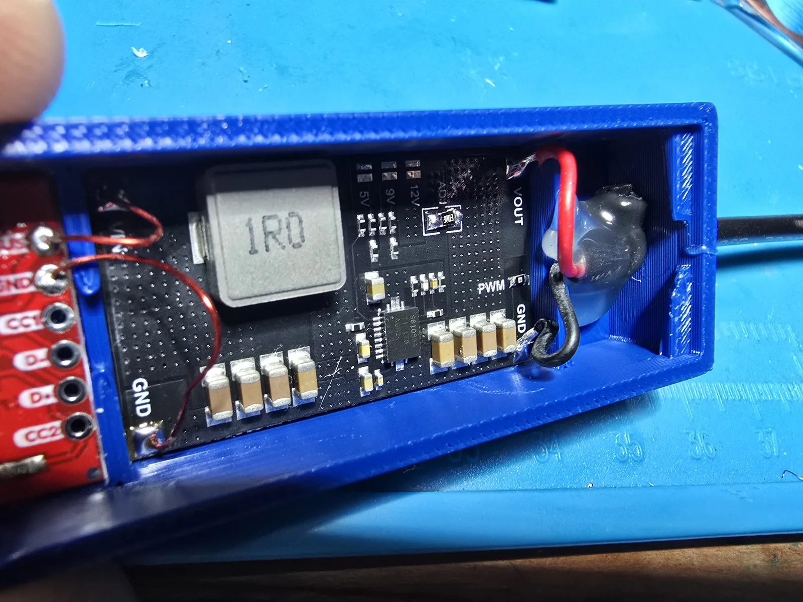 Inside the adapter: the boost converter board wired up with a zip tie and a hot-glue bead for cable strain relief