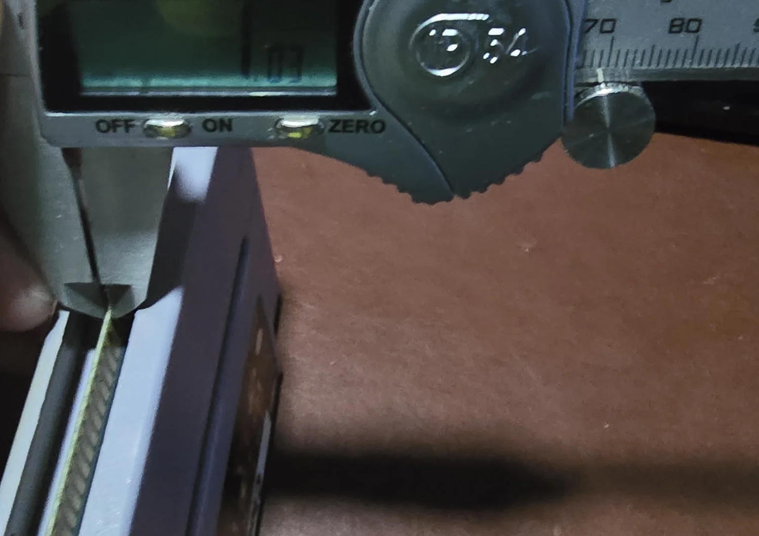 Digital calipers measuring the card edge of a cartridge, with the tapered outside jaws reaching into the shell opening and clamped across the gold contact fingers.