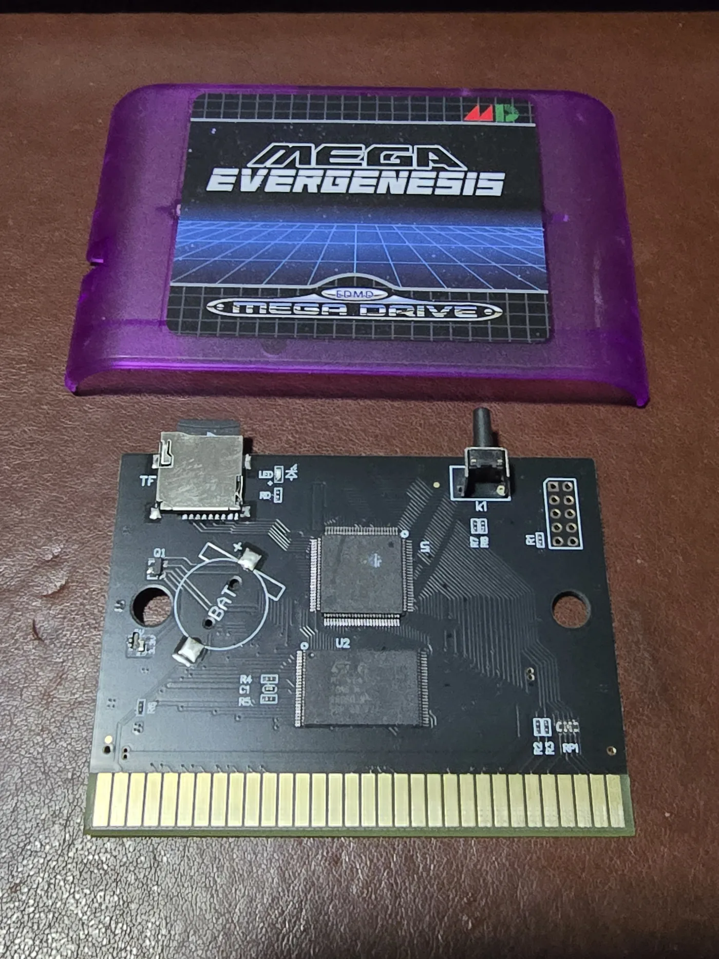 Mega EverGenesis flash cartridge board removed from its purple translucent shell, showing a microSD slot, a tactile button and a card edge connector.