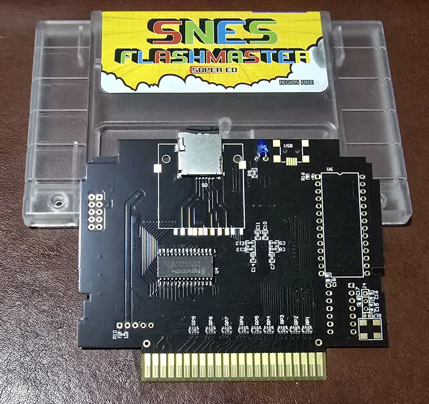 SNES FlashMaster Super ED cartridge in a clear shell, with a yellow label reading SNES FlashMaster Super ED Region Free, showing the black PCB with a microSD slot.