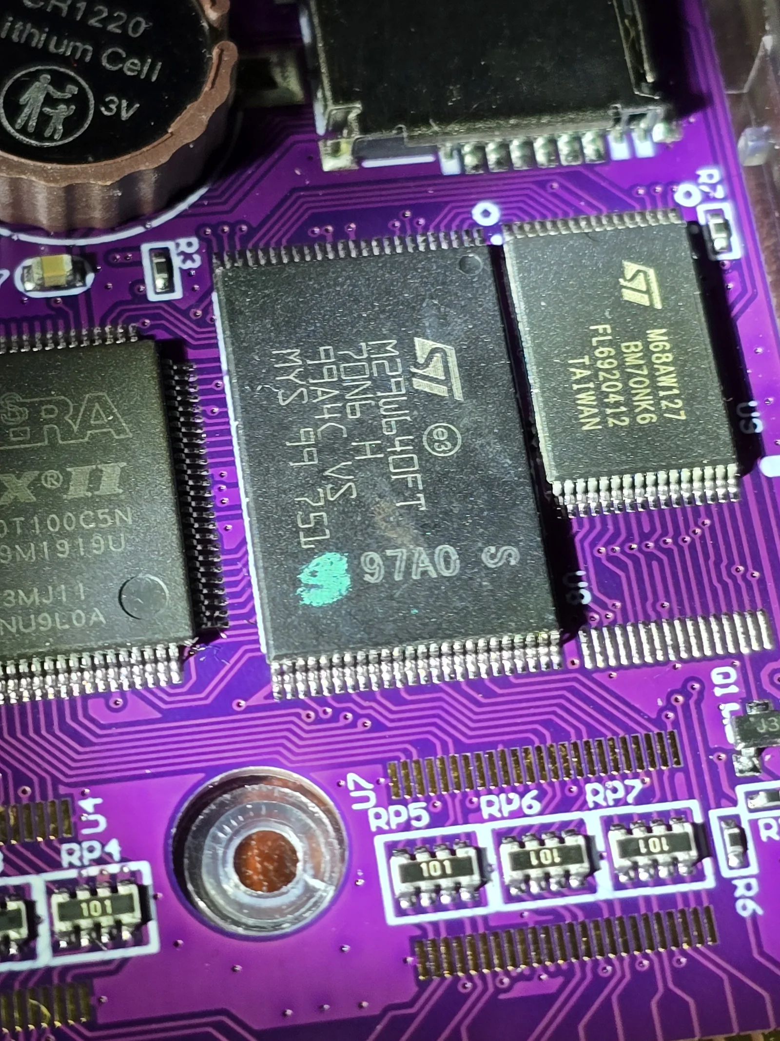 Close-up of the GB Pro+ board showing an ST M29W640FT flash chip at U8 and a smaller ST M68AW127 SRAM at U9 side by side, with the edge of the Altera MAX II EPM240T100C5N at the left and resistor networks RP5 to RP7 below.