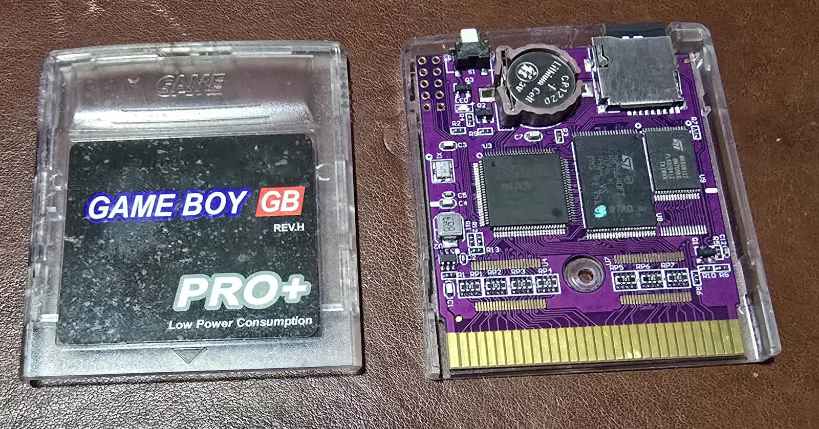 A Game Boy flash cartridge in a clear shell beside its purple PCB, the label reading GAME BOY GB PRO+ REV.H and Low Power Consumption, the board carrying a coin cell, a microSD socket, a large square CPLD and two memory chips.