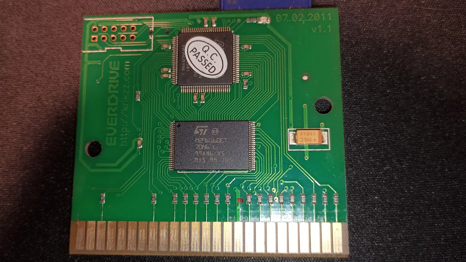 Master EverDrive cartridge PCB, whole board, showing a large QFP under a Q.C. PASSED sticker, an ST M29W160ET flash chip, and a row of about twenty small discrete resistors standing between the card edge fingers and the rest of the board.