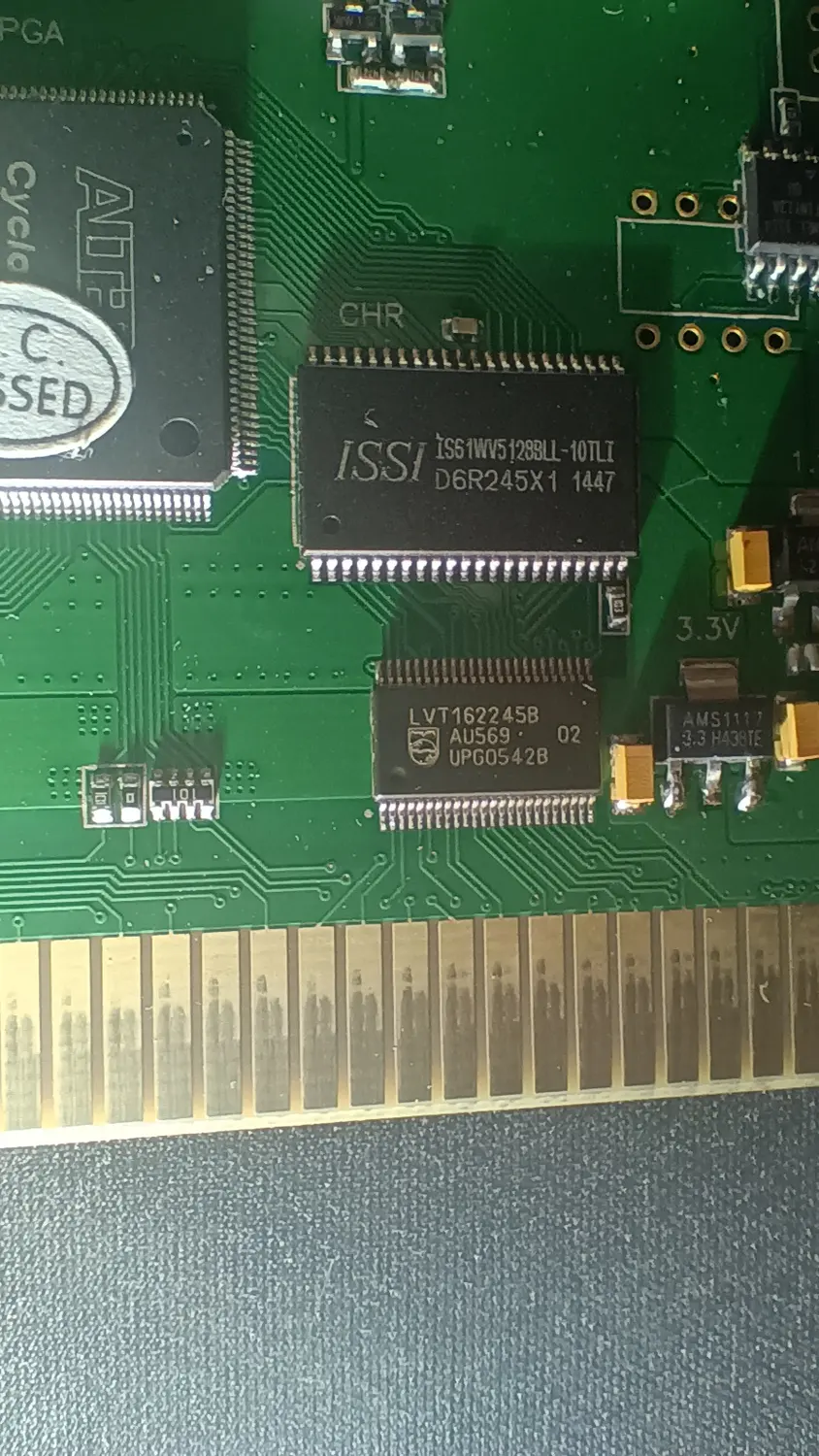 Close-up of an EverDrive N8 PCB showing an ISSI IS61WV5128BLL-10TLI SRAM labelled CHR on the silkscreen, a transceiver marked LVT162245B AU569 UPG0542B below it, an AMS1117 regulator beside a 3.3V silkscreen marking, and the card edge fingers along the bottom.