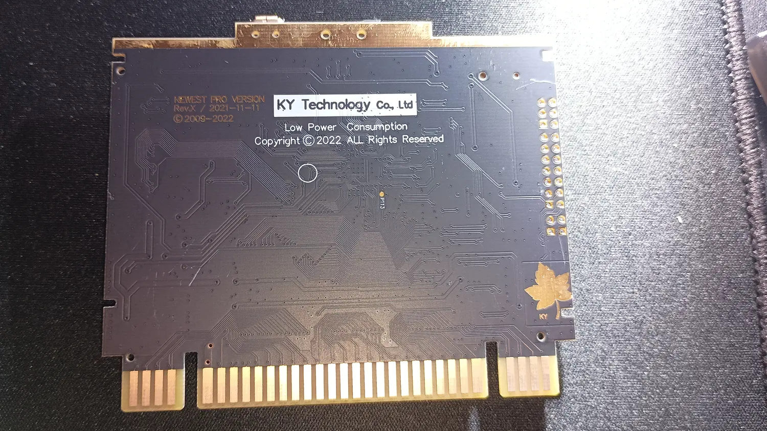 Solder side of an SD2SNES-style cartridge PCB showing a white printed sticker reading KY Technology Co., Ltd, Low Power Consumption, Copyright 2022 All Rights Reserved, next to silkscreen reading NEWEST PRO VERSION Rev.X 2021-11-11, with a gold maple leaf logo marked KY near the card edge.