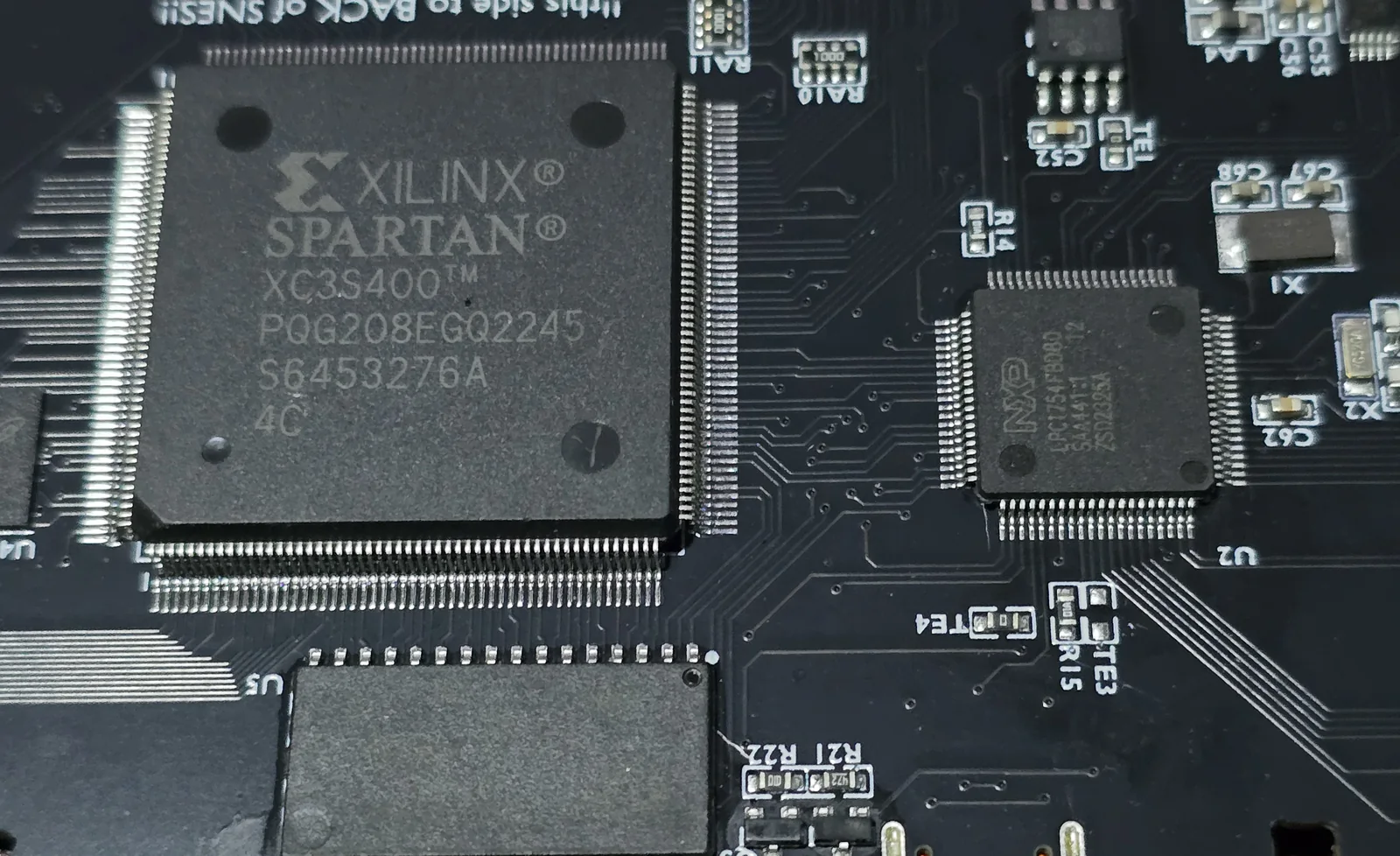 Close-up of the SD2SNES showing a Xilinx Spartan XC3S400 FPGA in a 208-pin package and an NXP LPC1754FBD80 ARM microcontroller.