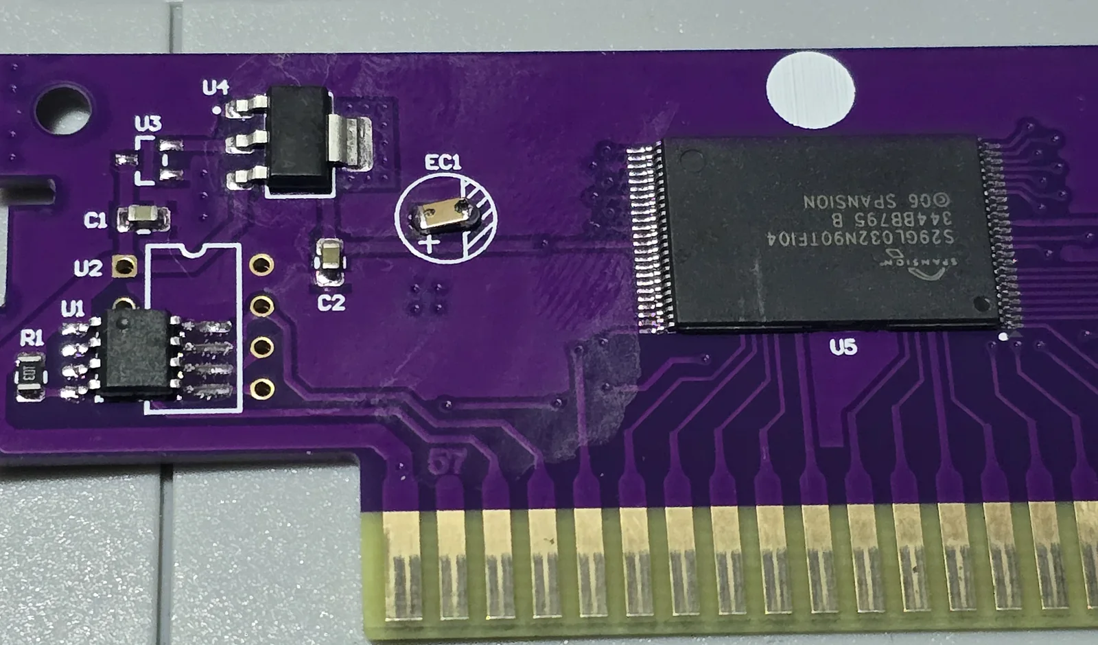 Close-up of the burn-in cartridge PCB showing a SOT-223 regulator at U4, an unmarked SOIC-8 at U1, unpopulated footprints at U2 and U3, and a Spansion TSOP flash chip at U5 marked S29GL032N90TFI04, with traces running directly from the card edge connector to the flash.
