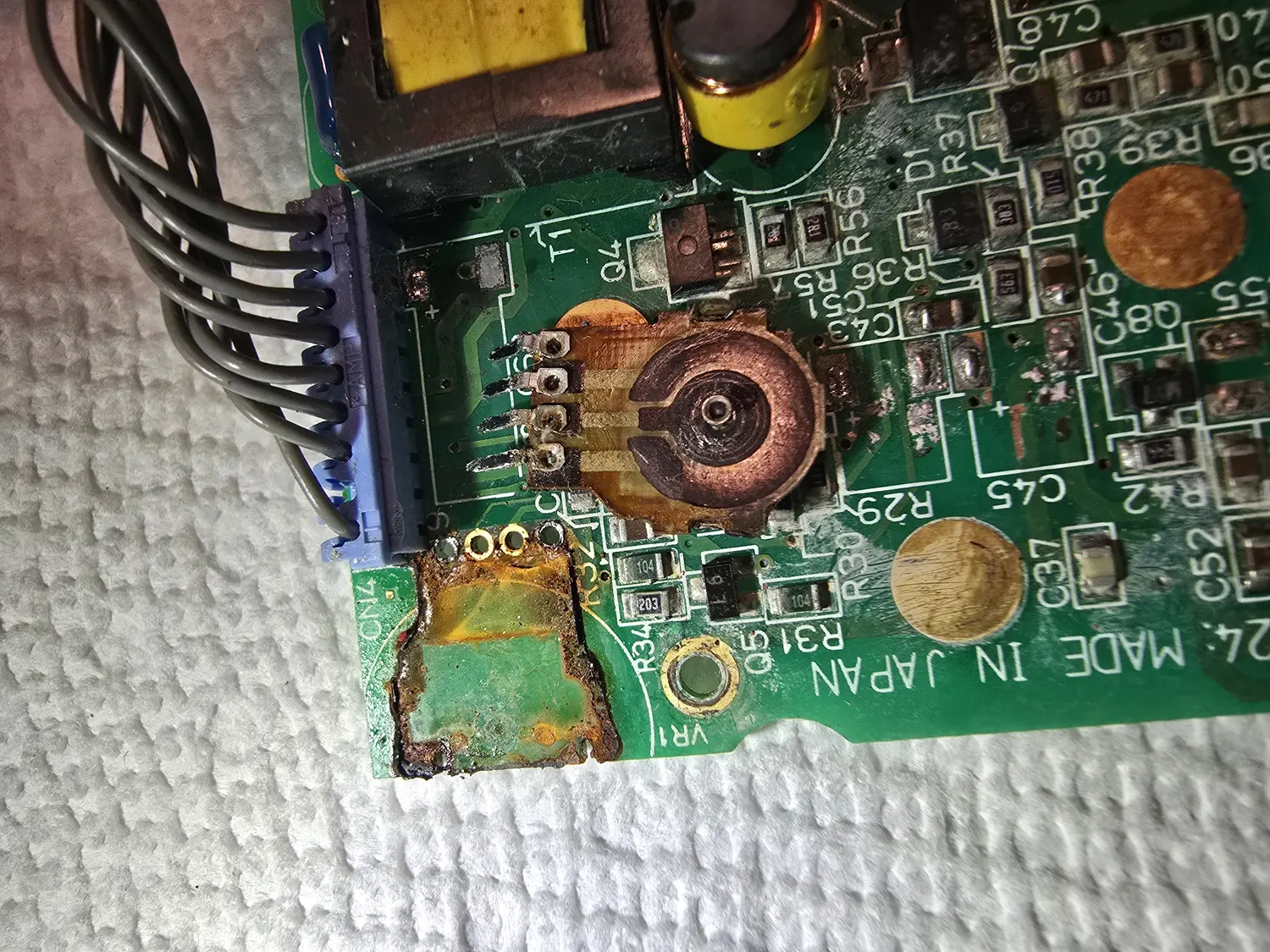 Close-up of a corroded Game Gear main board corner around the contrast potentiometer. The pot's exposed wheel and its terminals are green and black with corrosion, the solder mask around them has been eaten away leaving bare blackened laminate, and a blue multi-way connector sits at the left edge. Silkscreen visible nearby includes VR1, CN4, T1, Q4, R29, R30, C43, C45, C46 and MADE IN JAPAN.