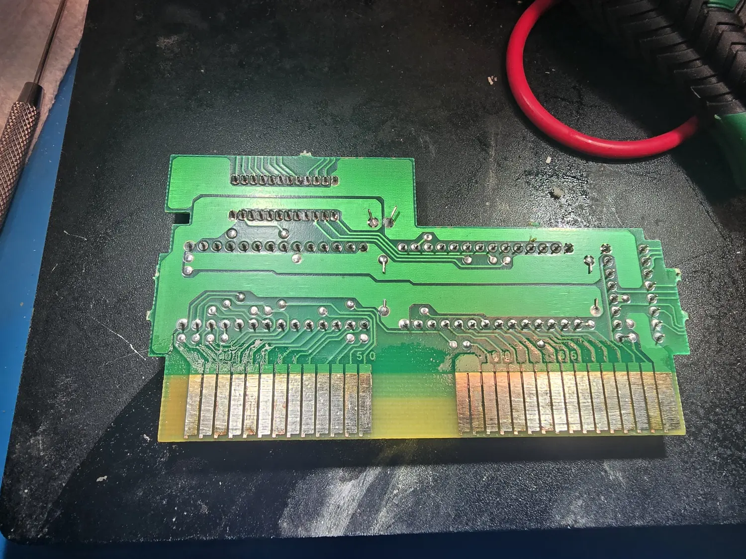 Solder side of the same NES cartridge board, showing rows of through-hole solder joints for the DIP chips on the other face, a silkscreened 50, and the 72-pin gold card edge along the bottom with visible tarnish and wear on the contacts.