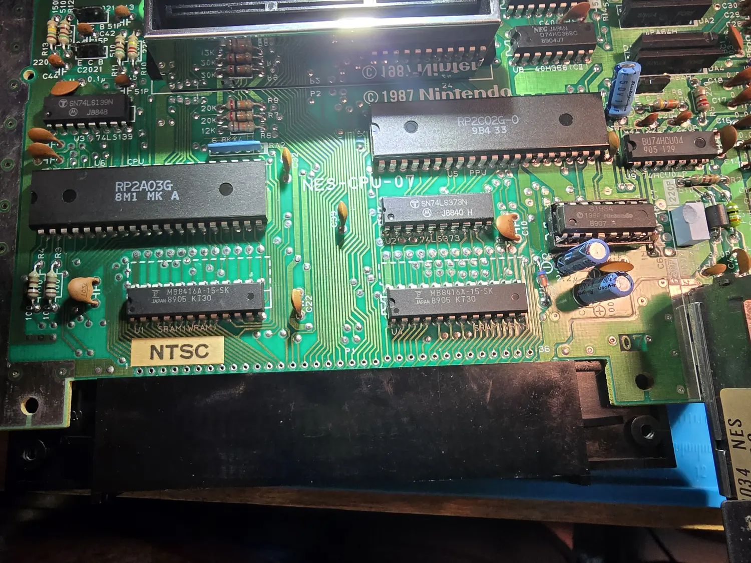 An NES-001 mainboard photographed from above, silkscreened NES-CPU-07 and copyright 1987 Nintendo. Labelled ICs include an RP2A03G CPU at U6, an RP2C02G-0 PPU at U5, two Fujitsu MB8416A-15-SK static RAMs at U1 marked SRAM(WRAM) and U11 marked SRAM(VRAM), an SN74LS139N at U3, an SN74LS373N at U2, a NEC D74HC368C and a 40H368 at U8, a BU74HCU04 at U9, and a 16-pin chip marked 3193A with a 1986 Nintendo copyright sitting in a machined socket. A hand-written NTSC label is stuck to the board near the cartridge connector.