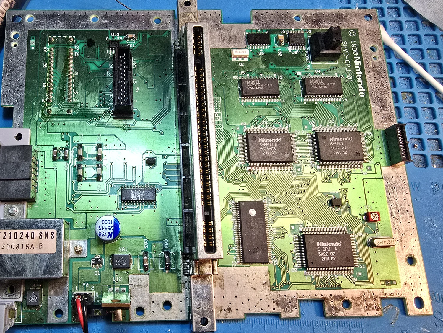 A Super Nintendo mainboard photographed from directly above with both RF shield cans removed, silkscreened SHVC-CPU-01 with a 1990 Nintendo copyright running up the right edge. Three separate Nintendo QFP chips sit to the right of the 62-pin cartridge slot: S-CPU A 5A22-02, S-PPU1 5C77-01 and S-PPU2 B 5C78-03, alongside two MOSEL MS62256CL-10FC SRAM chips and an S-WRAM chip. An S-ENC A BA6592F video encoder sits on the left half, and a metal RF modulator can marked E210240 SNS is still wired to the board at the left edge.
